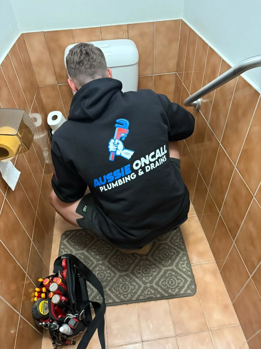 Plumber repairing a toilet in a tiled bathroom